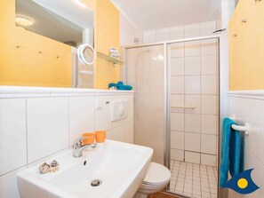 Une salle de bain avec un lavabo blanc, un miroir et des toilettes. On y trouve une douche en verre et un porte-serviettes avec une serviette bleue.