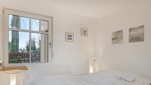 Een hotelkamer met een groot bed, een nachtkastje, een raam met uitzicht op bomen en een gebouw, en twee foto's in lijsten aan de muur.