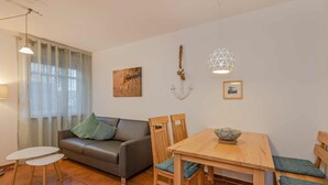 Een woonkamer met een bank, een eettafel met stoelen, een klein wit tafeltje en een wandlamp.