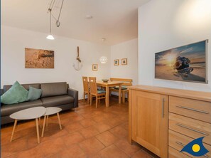 Un salon comprenant un canapé, une table à manger avec des chaises, un téléviseur et un meuble.