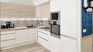 Een moderne keuken met witte kasten, een inbouwoven, een magnetron en een koffiezetapparaat.