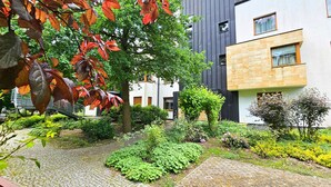 Een binnenplaats met een geplaveid pad, een boom met herfstbladeren en moderne gebouwen met grote ramen.