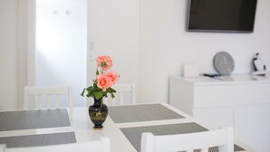 A white dining area with a table, chairs, and a vase with flowers. - Serious Job Apartment (Dubrovnik)