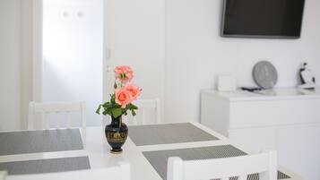 A white dining area with a table, chairs, and a vase with flowers.