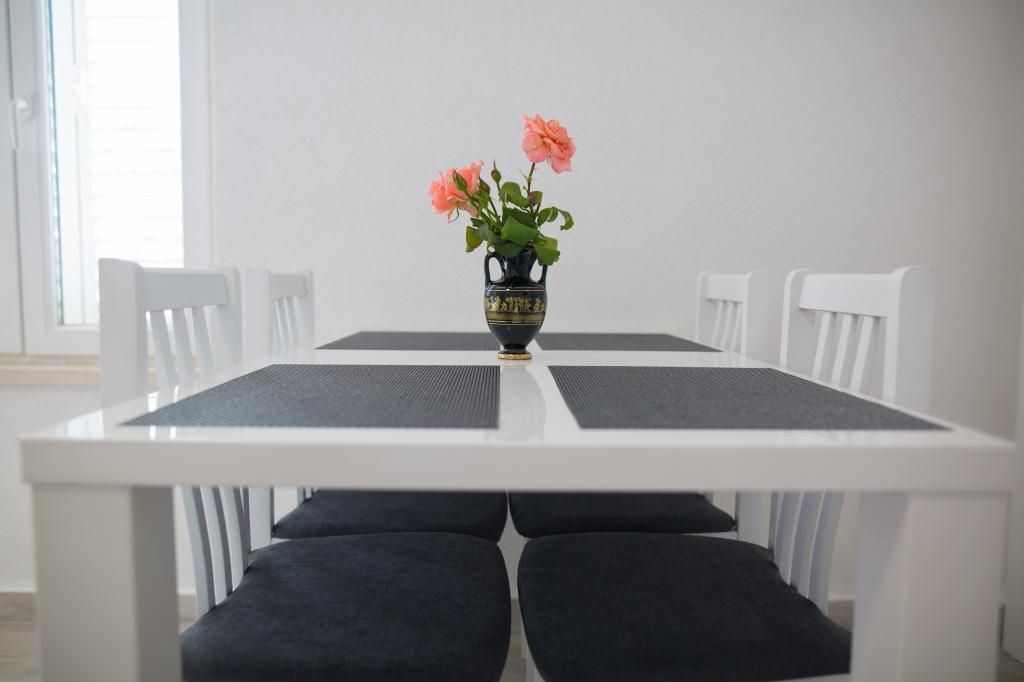 Et spisebord med en blomstervase, omgivet af hvide stole.