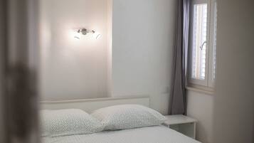 Une chambre à coucher comprenant un lit, une table de chevet, un luminaire fixé au mur et une fenêtre avec des rideaux.