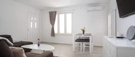 A modern living room with a sofa, a small table, and a dining area with chairs.