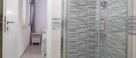 A modern bathroom with a shower, tiled walls, and a small bedside table.