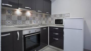 Une cuisine moderne avec des meubles de couleur sombre, un réfrigérateur blanc, un four à micro-ondes et un four traditionnel.
