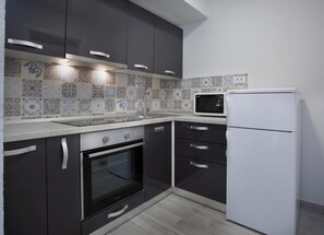 A modern kitchen with dark cabinets, a white refrigerator, a microwave, and an oven. - Serious Job Apartment (Dubrovnik)