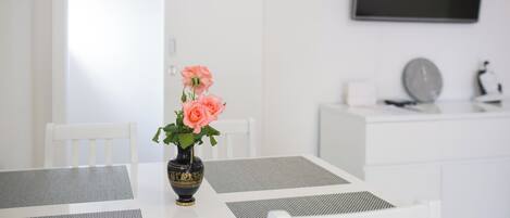 A white dining area with a table, chairs, and a vase with flowers.