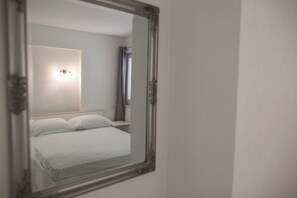 A bedroom with a bed, a nightstand, a wall-mounted light, and a mirror. - Serious Job Apartment (Dubrovnik)