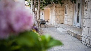 A courtyard with a table and chairs, a white door, and a stone wall. - Serious Job Apartment (Dubrovnik)