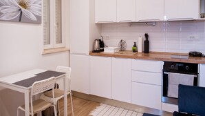 A modern kitchen with white cabinets, a wooden countertop, a sink, and a dining area with a table and chairs. - Serious Job Apartment (Dubrovnik)