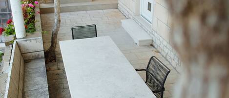 Un espace patio avec une table blanche et deux chaises, un arbre et une porte blanche.