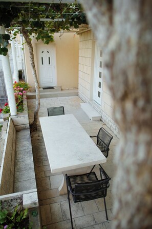 A patio area with a white table and two chairs, a tree, and a white door. - Serious Job Apartment (Dubrovnik)
