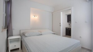 A bedroom with a bed, a nightstand, a wall-mounted light, and a door leading to a bathroom. - Serious Job Apartment (Dubrovnik)