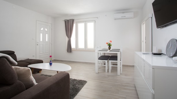 A modern living room with a sofa, a small table, and a dining area with chairs. - Serious Job Apartment (Dubrovnik)