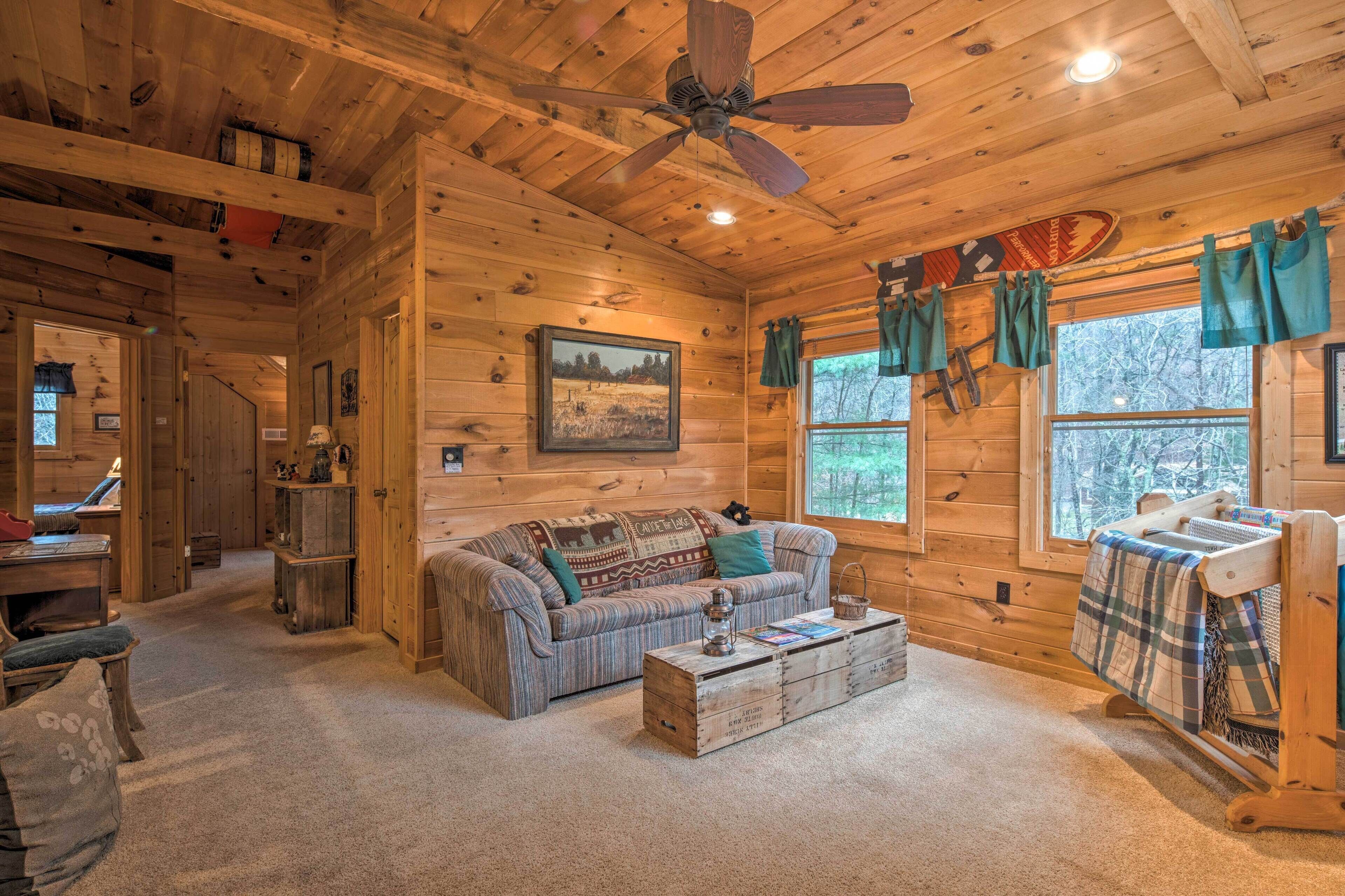 A cozy cabin interior with a wooden ceiling, a ceiling fan, a sofa, a coffee table, and a window with curtains.