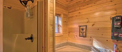 A wooden cabin bathroom with a bathtub, a shower, and a window with blinds.
