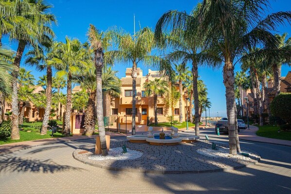A courtyard with palm trees, a fountain, and a building with balconies.