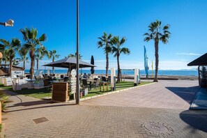 Een terras aan het strand met buiten zitplaatsen, palmbomen en uitzicht op de oceaan.