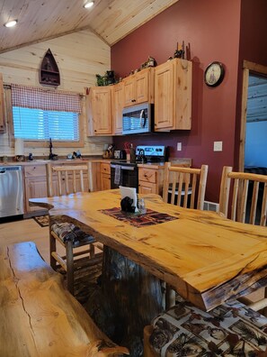 A rustic kitchen with wooden cabinets, a large wooden table, and a clock on the wall.