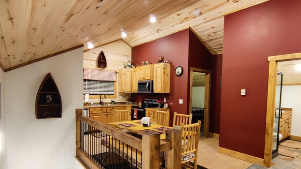 Un intérieur en bois avec un escalier menant à une salle à manger, une cuisine dotée de meubles en bois et un mur d’accent rouge.