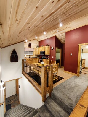 Un interno in legno con una scala che conduce a una sala da pranzo, una cucina con mobili in legno e una parete rossa a contrasto.