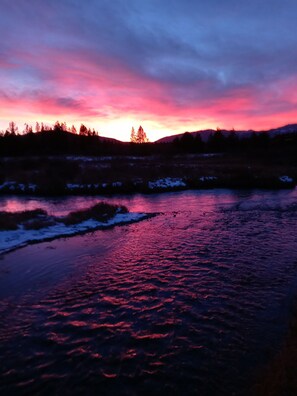 A river reflecting a sunset with a forested hillside in the background.