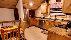 Une cuisine chaleureuse avec des meubles en bois, un réfrigérateur, un évier et un coin repas comprenant une chaise et une table.