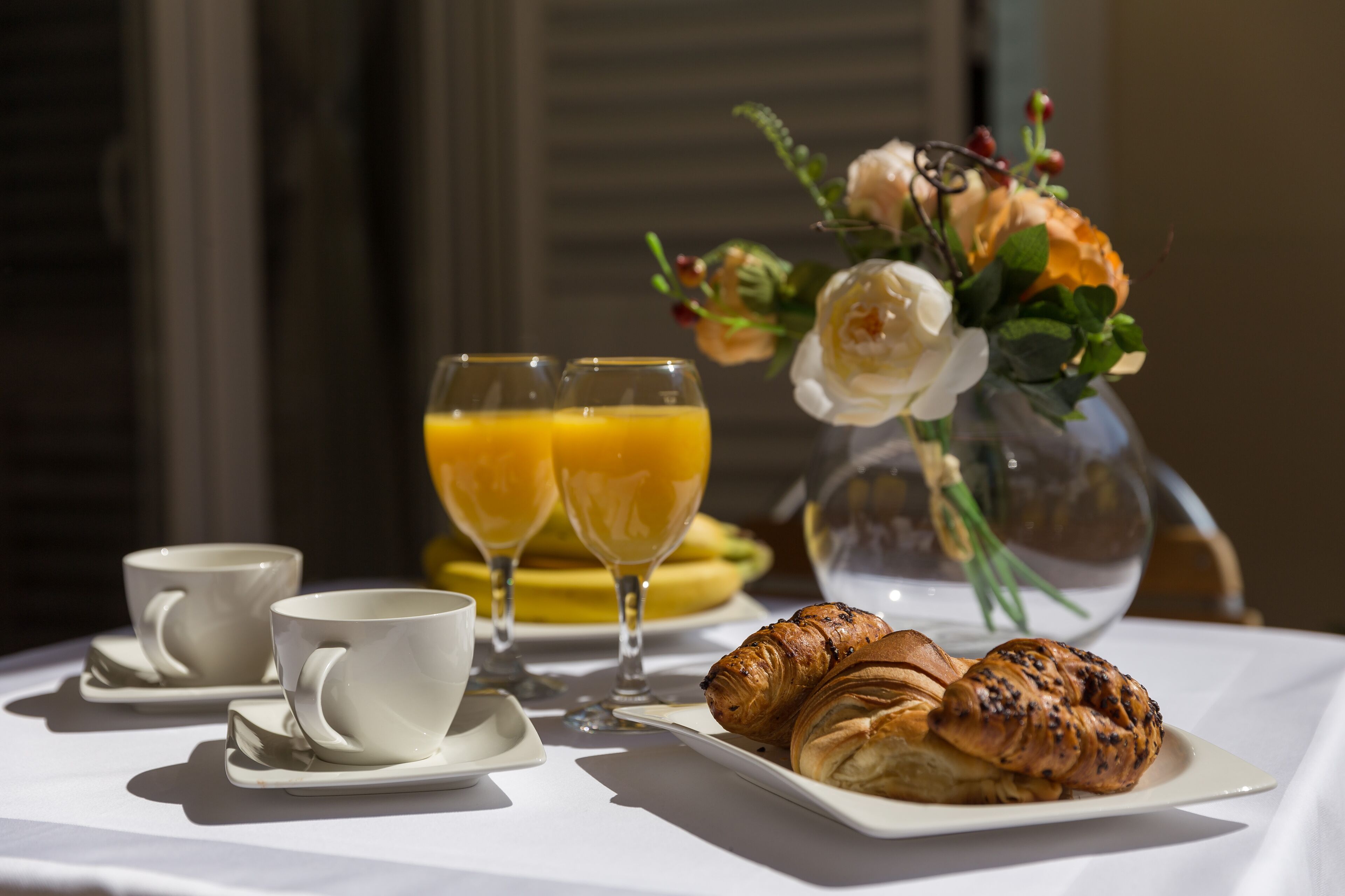 Un desayuno con cruasanes, jugo de naranja y tazas de café sobre una mesa.