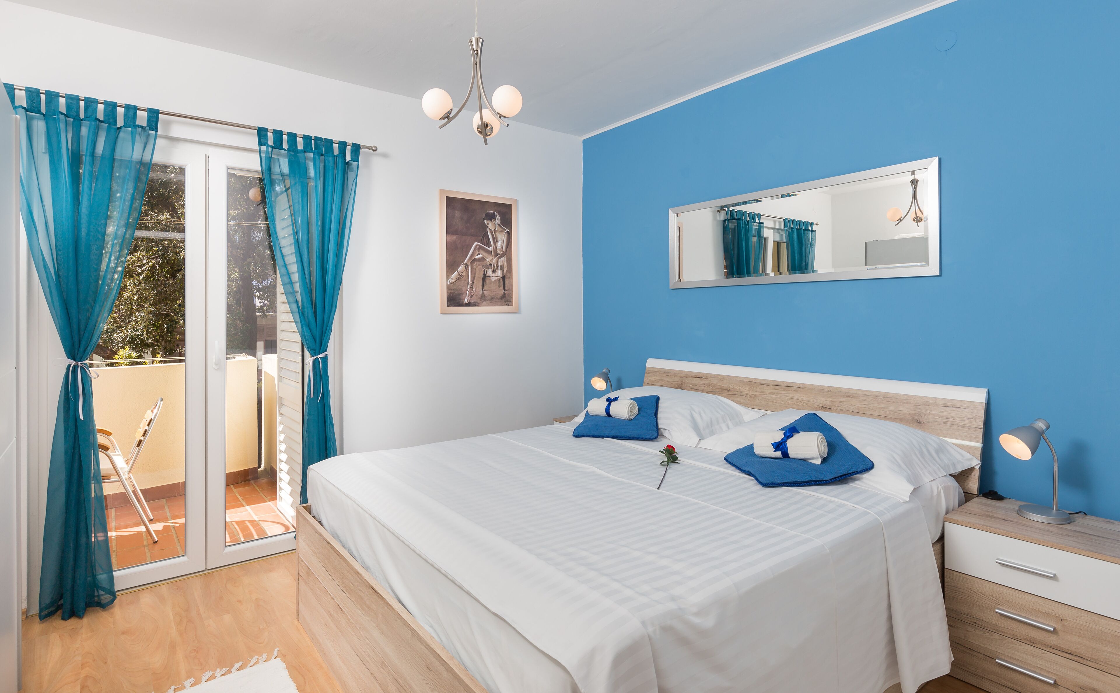 Quarto com cama, mesa de cabeceira, espelho e vista para o exterior.