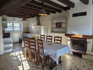 A dining area with a table, chairs, a fireplace, and a kitchen in the background.