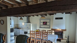 Een gezellige woonkamer met een open haard, een eethoek met houten stoelen, een keuken met witte kasten en een betegelde vloer.
