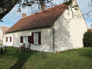 A white building with a red roof, a small table, and two chairs in front.