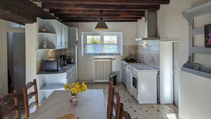 Een kleine keuken met witte kastjes, een raam en een betegelde vloer.