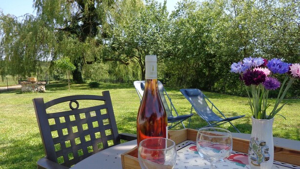Een buitentafel gedekt, met een fles, glazen en een bloemenvaas.