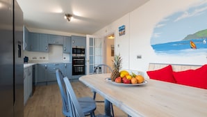 A modern kitchen with blue cabinets, a dining area with a wooden table, and a beach mural on the wall.