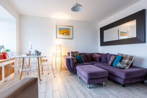 A modern living room with a sectional sofa, a dining table, and a large mirror on the wall.