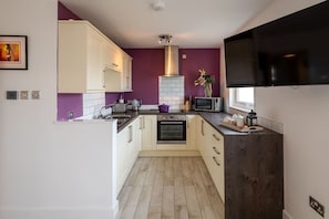 A compact kitchen with white cabinets, a microwave, an oven, and a dark wood countertop. - Sunset View: Two bedroom pet-friendly holiday apartment (Rhosneigr)