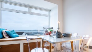 A modern kitchen with a large window, clear chairs, and a white table with a candle. - Headline (VRBO): Sunset View : Pet-Friendly 2‑Bed Apartment with Bay Views in Rhosneigr | Managed by (Rhosneigr)