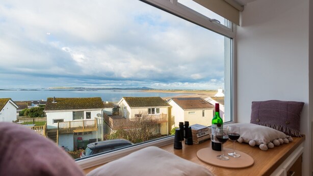A room with a view of a coastal area, a wooden table with a bottle of wine, glasses, and binoculars. - Headline (VRBO): Sunset View : Pet-Friendly 2‑Bed Apartment with Bay Views in Rhosneigr | Managed by (Rhosneigr)