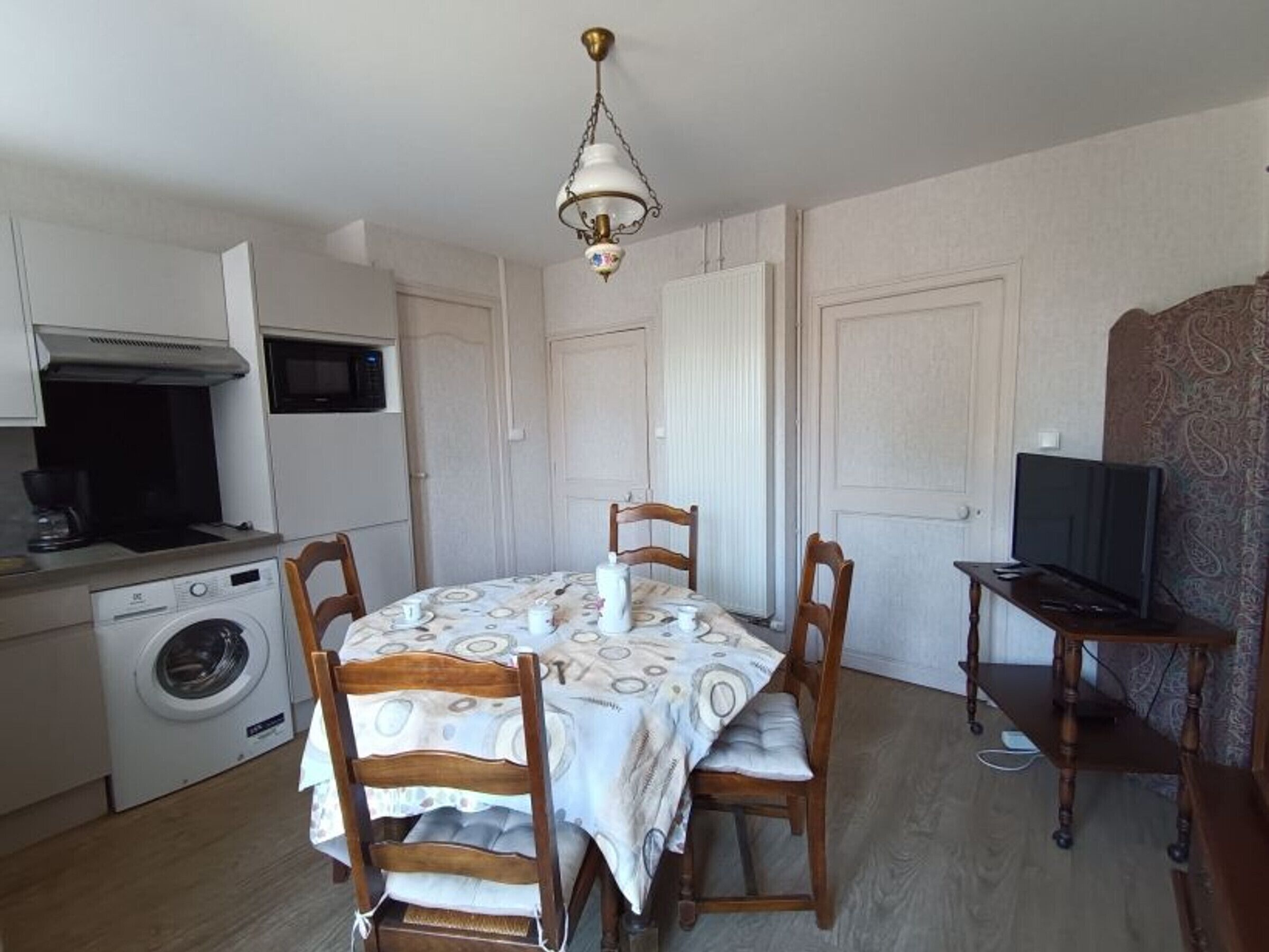 Une cuisine compacte équipée d’un lave-linge, d’un four à micro-ondes et d’un coin repas avec une table et des chaises.