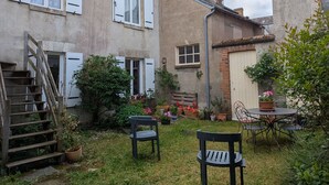 A rustic courtyard with a wooden staircase, two black chairs, and a small round table.