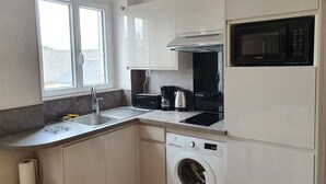 A compact kitchen with a built-in microwave, toaster, kettle, and washing machine.