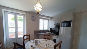 A compact kitchen with a dining table, chairs, a clock, a microwave, and a washing machine.