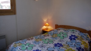 Een slaapkamer met een bloemenbedekker, een bedlamp en een raam met uitzicht op gebouwen.