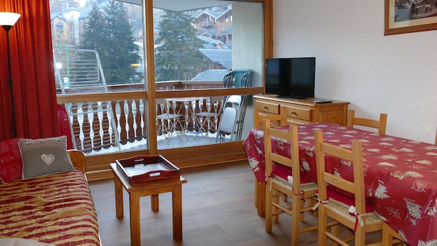 Een gezellige kamer met een bed, een klein tafeltje, een televisie en een balkon met stoelen.