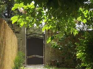 A rustic gate with a decorative top, surrounded by lush greenery and a stone wall. - Charming Country House between Paris & Orléans with Private Garden and Modern Amenities (Audeville)